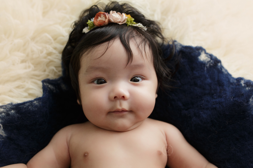 Milwaukee photographer photographs baby during her milestone session on a cream flokati wearing this adorable floral headband.