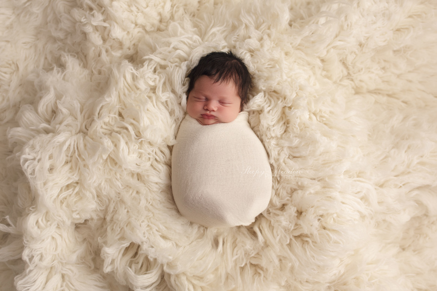Newborn baby posed on cream rug wrapped snuggly at Sleepy Meadow Photography.