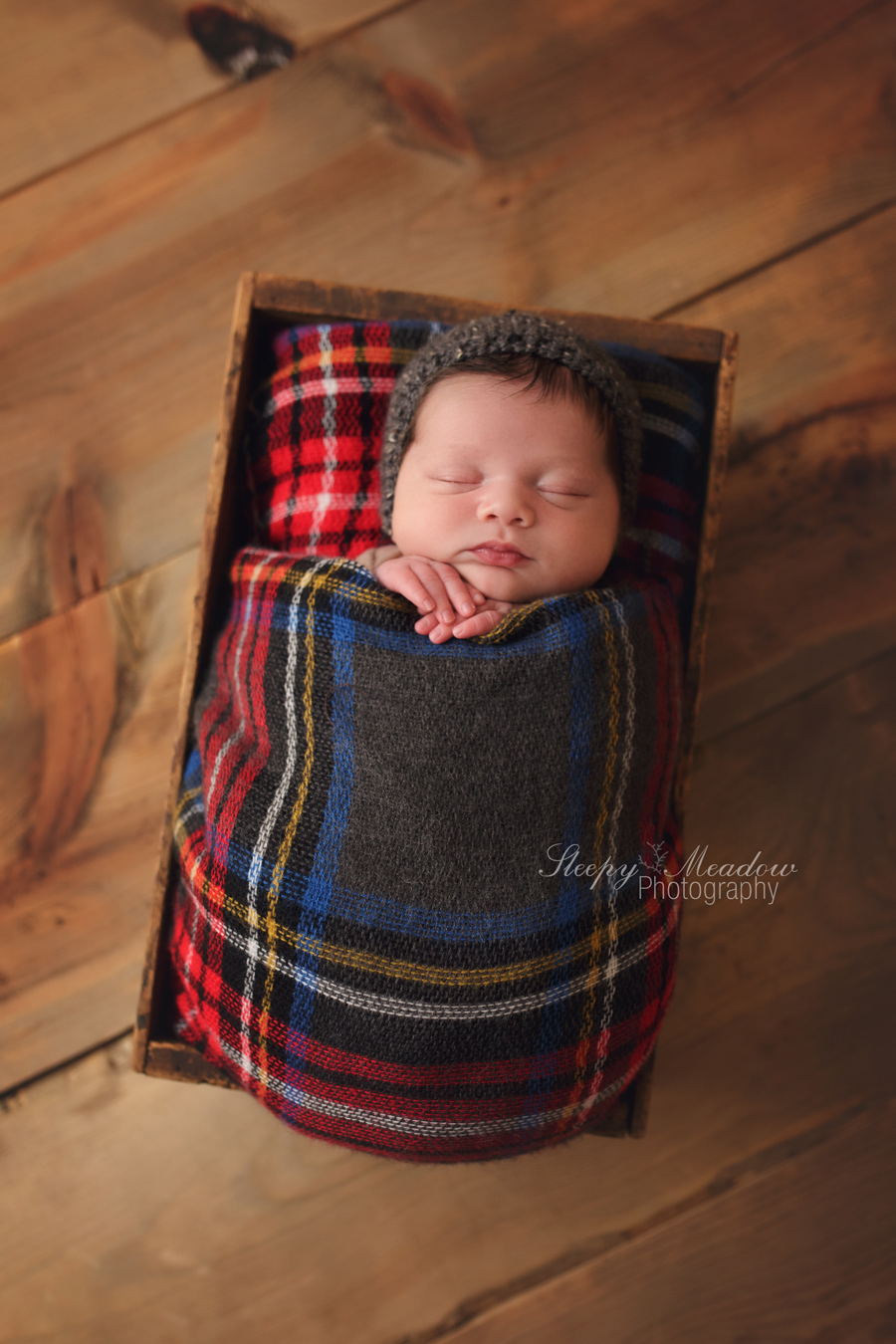 Newborn boy poses in a box for his first photo shoot by Sleepy Meadow Photography.