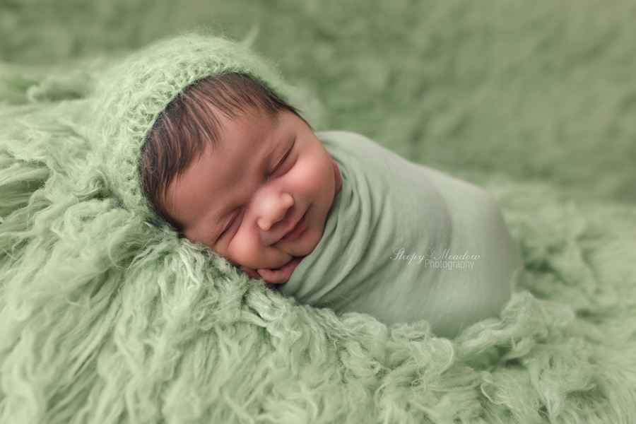 Baby boy smiling during his newborn session wearing a green bonnet by Sleepy Meadow Photography during his newborn session in Milwaukee.