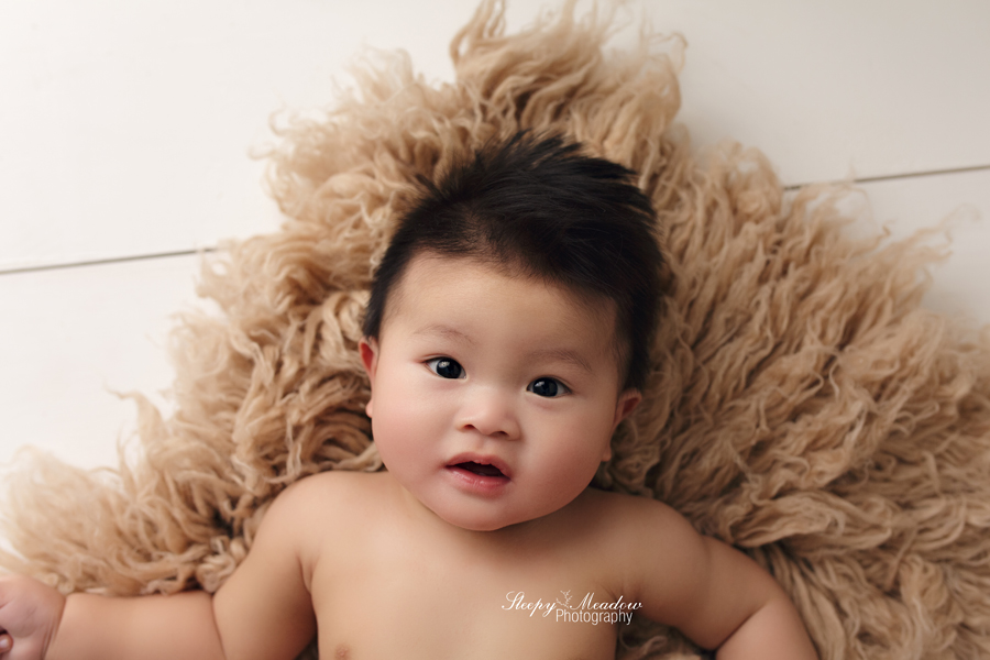 Beautiful baby boy poses on a neutral flokati for his baby session.