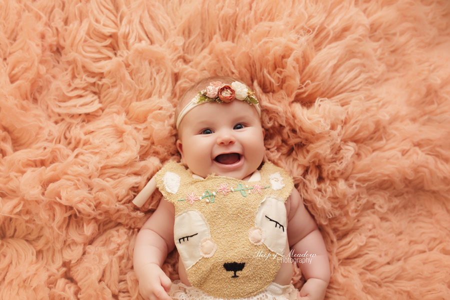 Happy baby girl photographed in a custom made fawn outfit on a peach colored flokati rug in Waukesha County portrait studio by Sleepy Meadow Photography.