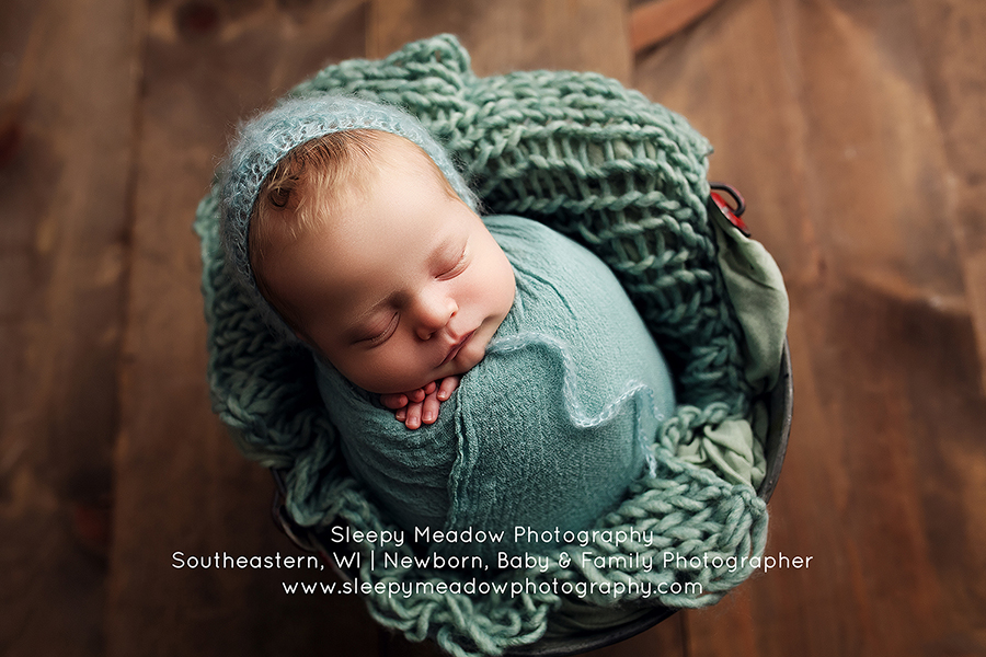 Baby wrapped in teal poses in a bucket for his newborn session with Sleepy Meadow Photography.