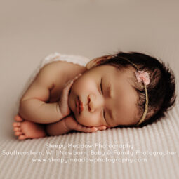 Adorable baby girl with headband has hands holding her cheeks.