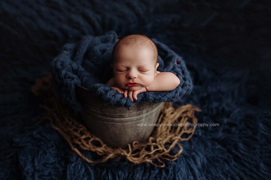 Newborn baby in a bucket with blue knit fabric.