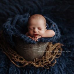 Newborn baby in a bucket on blue rug.
